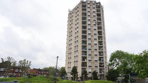 A tall beige tower block sits just behind a child's playground.