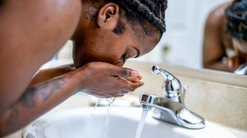 A woman washing her face over a sink