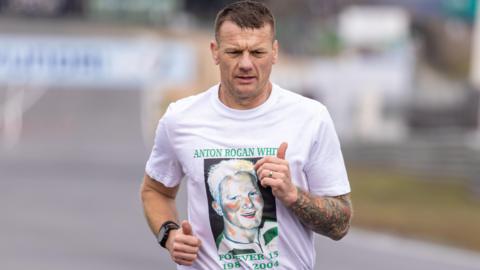 Bobby White, pictured from the waist up, wearing a t-shirt featuring his late brother's image. He is running and looking at the ground with a furrowed brow.