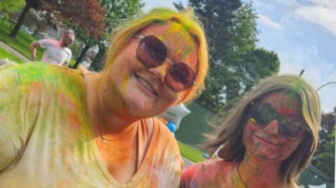 Two women with sunglasses covered in multi-coloured paints