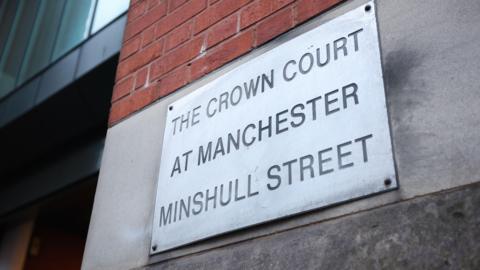 A metal sign botled to a concrete wall engraved with the words .The Crown Court at Manchester Minshull Street'.
