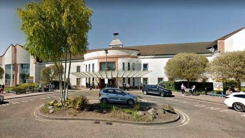 The entrance to University Hospital Wishaw, a hospital building with cars driving past 