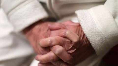 A stock image of an elderly person crossing their fingers together.