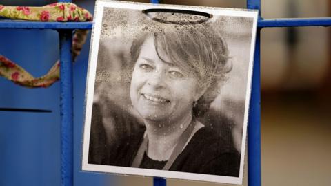 A photograph of Ruth Perry attached to the fence outside John Rankin Schools in Newbury, Berkshire. There are drops of rain on it.
