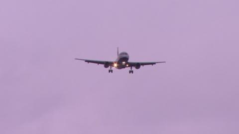 A plane with lights on coming into land with a grey sky behind it