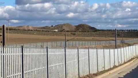 The waste recycling facility at Hacking Lane, South Elmsall. Large mounds of earth can be seen in the distance behind a metal fence.