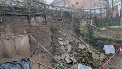 The collapsed section of Chester's walls. Debris, including large slabs, is scattered down a steep slope.