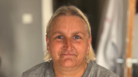 Natasha Robinson smiles at the camera. She has short blonde hair and wears a grey top. 