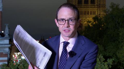 Chris Mason standing with the witness statements printed on a pile of paper in Westminster