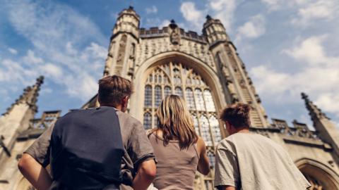 Three GCSE students on a history field trip look up at a cathedral against a blue sky.