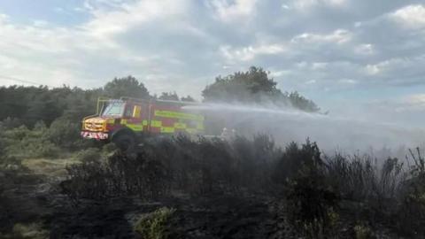 A fire engine spraying burning heathland with water