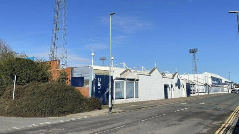 The outside of a small football ground with white and blue walls