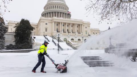 A worker removes snow from a sidewalk outside the US Capitol in Washington, DC.