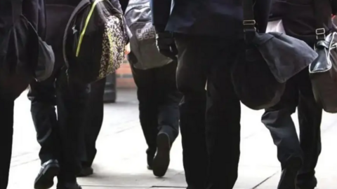 A stock image of the backs of pupils, from the shoulders down. They are wearing black school uniform and carrying bags