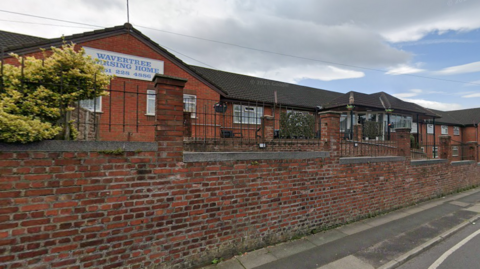 Exterior shot of Wavertree Nursing Home in Liverpool. It is a one-and two-storey complex built in red brick and running along a main road. 