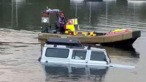 A rescue boat sails behind the partly submerged car in Windermere