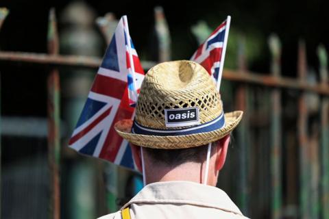 Rear view of a man wearing a straw sun hat branded with the black and white Oasis logo and union flags on either side of his hat