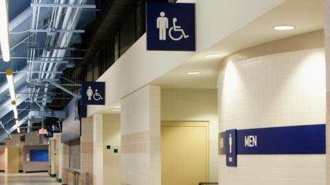 A sign for male, female and disabled toilets running along a corridor in a stadium. 