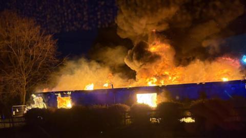 A single story building engulfed in flames that are lighting up the night sky