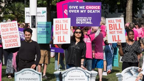 People holding up signs for and against the assisted dying bill