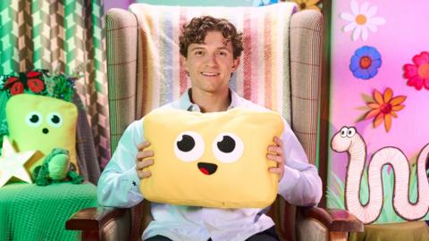 Tom Holland holding a yellow cushion with a smiley face on it