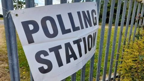 A sign for a polling station attached to a metal fence