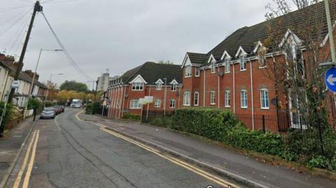 A screenshot from Google street view showing a residential road with houses on either side, and double yellow lines running next to the kerbs.