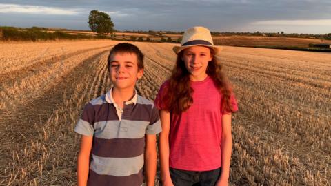 A boy and a girl standing in a field the crops have been cut