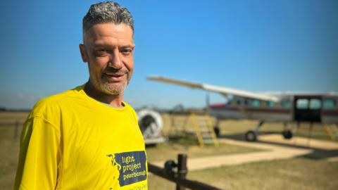 Dan Perkins wearing a yellow T-shirt standing in front of a plane