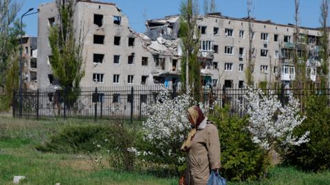 A woman walks from a church during Orthodox Easter celebrations, as an apartment building damaged in the course of Russia-Ukraine conflict is seen in the background, in Avdiivka (Avdeyevka), in the Donetsk region, a Russian-controlled area of Ukraine, April 20