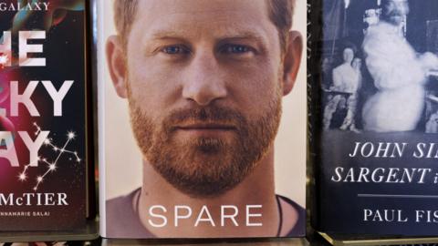 The cover of Prince Harry's book, titled Spare features a closeup photo of the prince looking directly at the camera. The book is displayed between two others.