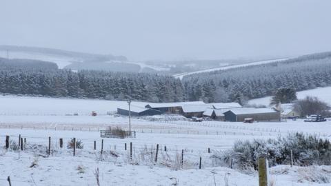 Farm, farm buildings and trees with a light covering of snow.