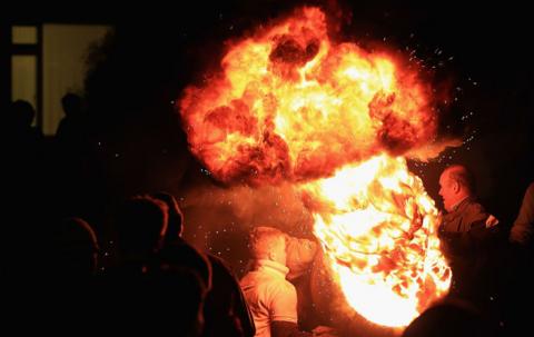 People watch as a burning barrel soaked in tar is carried at the annual Ottery St Mary Tar Barrel fe