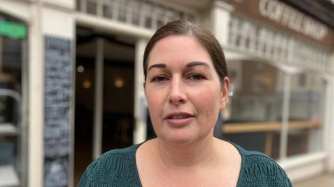 Manager Hannah Lewis wearing green standing in front of the premises