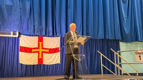 A man reading out results on a stage.