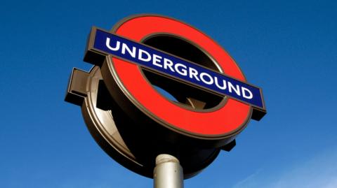 London Underground sign in London, blue sky seen behind. 