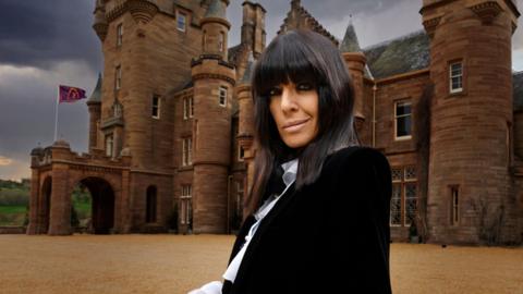 Claudia Winkleman in front of The Traitors castle