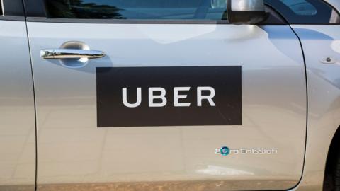 A silver car with an Uber symbol on its driver's door and a zero emissions badge in the bottom right-hand corner of the door.