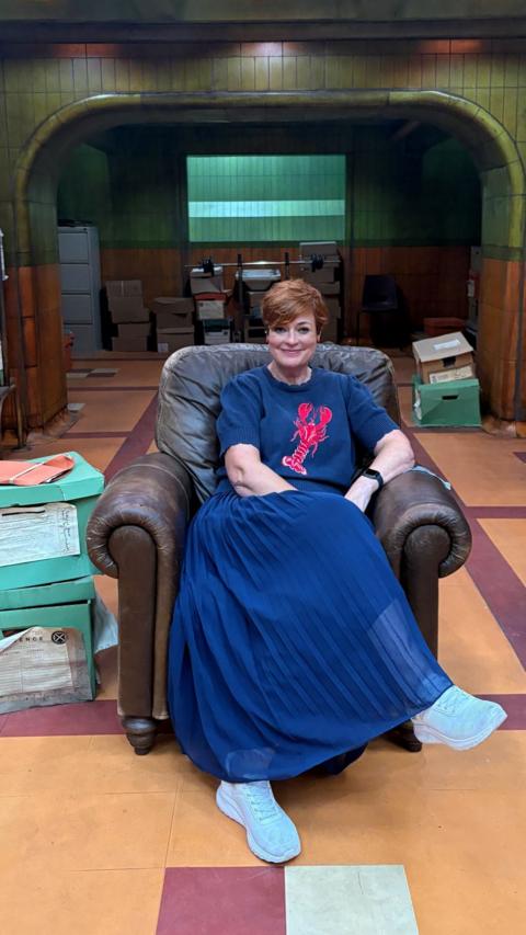 Woman with blue skirt and auburn short hair smiling