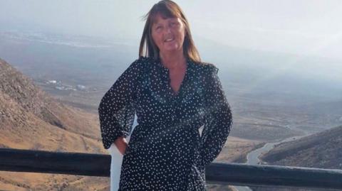 Anita Ashcroft, wearing a dark blue dress with small white spots, poses for a photo high above a stunning valley