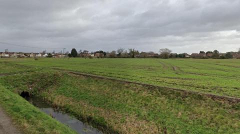 A green field with some houses on the edges. 