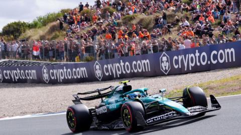 Aston Martin's Fernando Alonso passes a sandbank where fans watch the action at Zandvoort