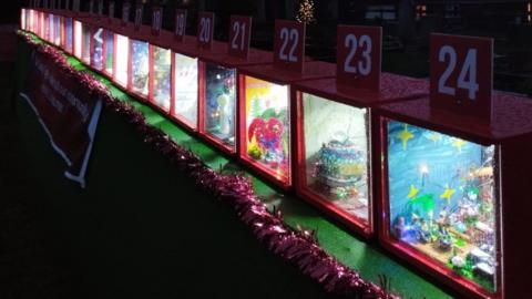 The advent calendar is shown. It is 24 red boxes with Christmas themed arts and crafts inside. There is tinsel lined on the wall also.