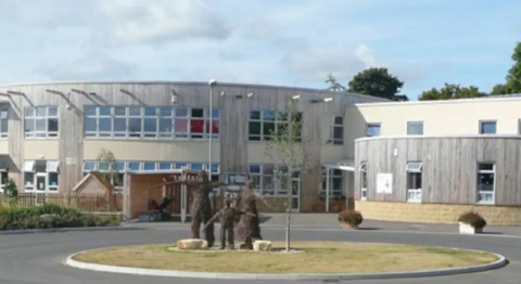 A rounded grey building with a grassy roundabout in front. there are three brown figures on top