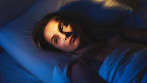 A woman lies in bed at night looking pensive