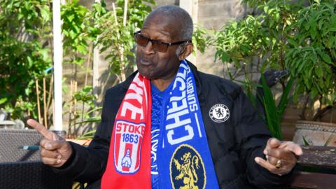 Raymond James wearing a Chelsea Football Club coat and a football scarf