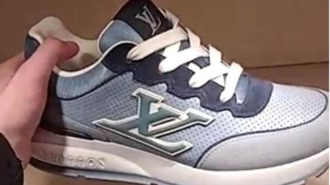 A hand is holding a trainer which is blue and white and has the letters "XL" on one side