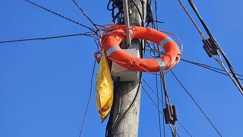 An orange rescue buoyancy ring caught high up on a telegraph pole, surrounded by cables.