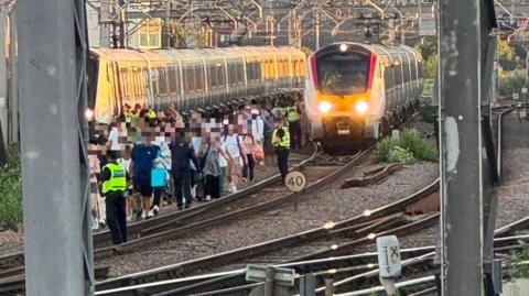 A group of people in single file walk along a train track. 