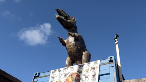 A metal dinosaur on top of a shipping container garage